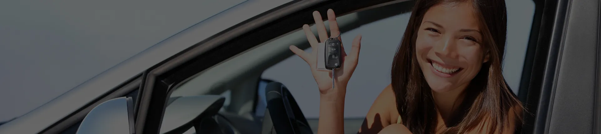 A girl smiling from inside a car and showing the keys of the car